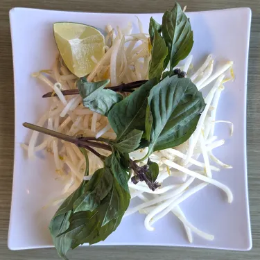 A plate of herbs used to top beef noodle soup