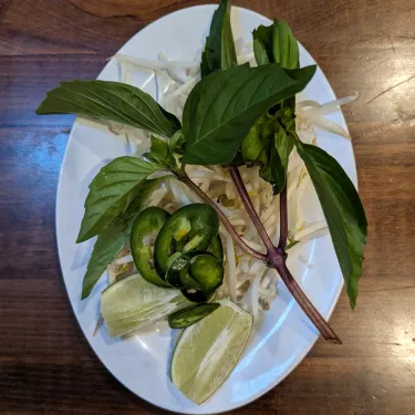 A plate of herbs used to top beef noodle soup