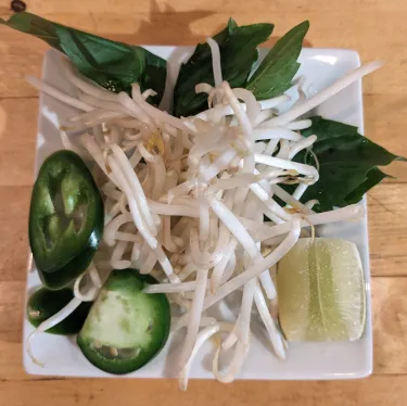 A plate of herbs used to top beef noodle soup