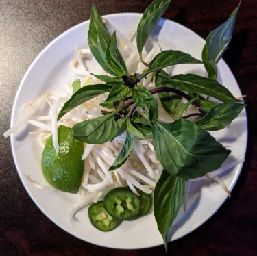 A plate of herbs used to top beef noodle soup