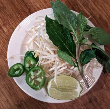 A plate of herbs used to top beef noodle soup