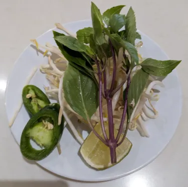 A plate of herbs used to top beef noodle soup