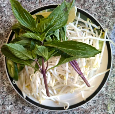 A plate of herbs used to top beef noodle soup