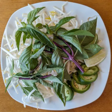 A plate of herbs used to top beef noodle soup